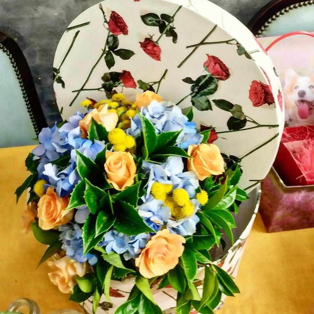 Cappelliera decorata piena di ortensie azzurre, rose pesca e achillee gialle