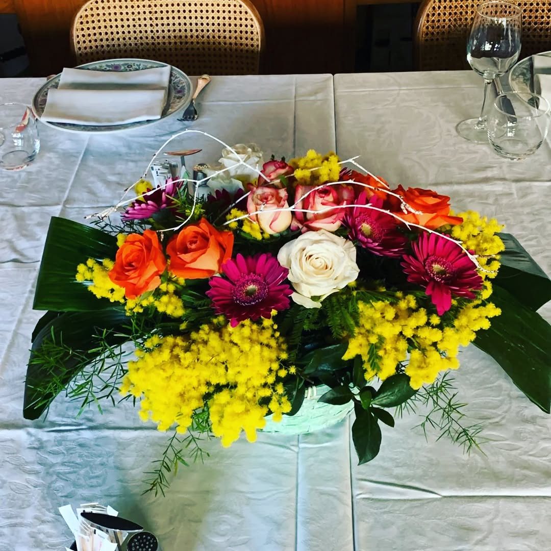 Centrotavola con mimosa, rose e gerbere su una tavola apparecchiata